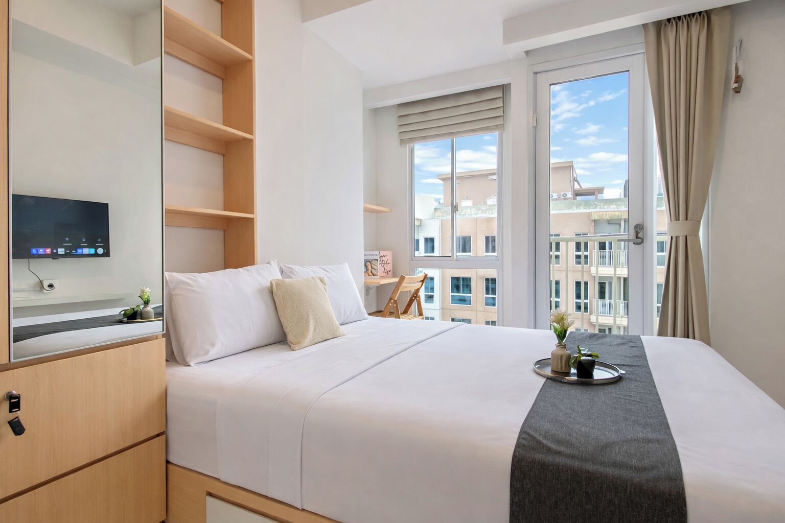 Una camera d'albergo con un letto, una televisione, una finestra con tende e vista sulla città.