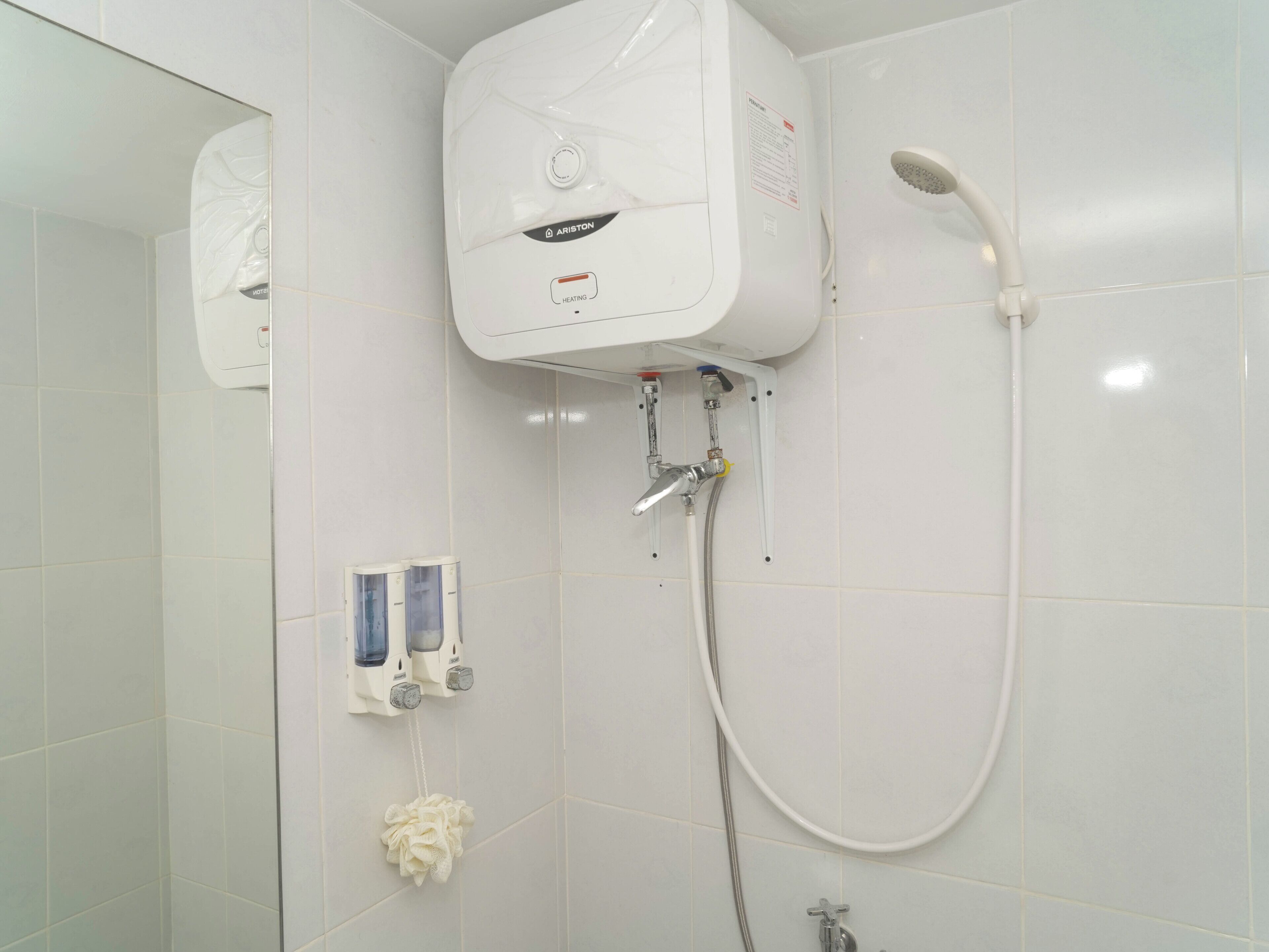 A bathroom with a white tiled wall, a white shower unit, a handheld showerhead, and a wall-mounted hand dryer.