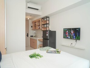 A modern hotel room with a bed, a TV, a kitchenette, and a window. - Nice Studio With Comfort At Apartment Tokyo Riverside Pik 2 (Teluknaga)