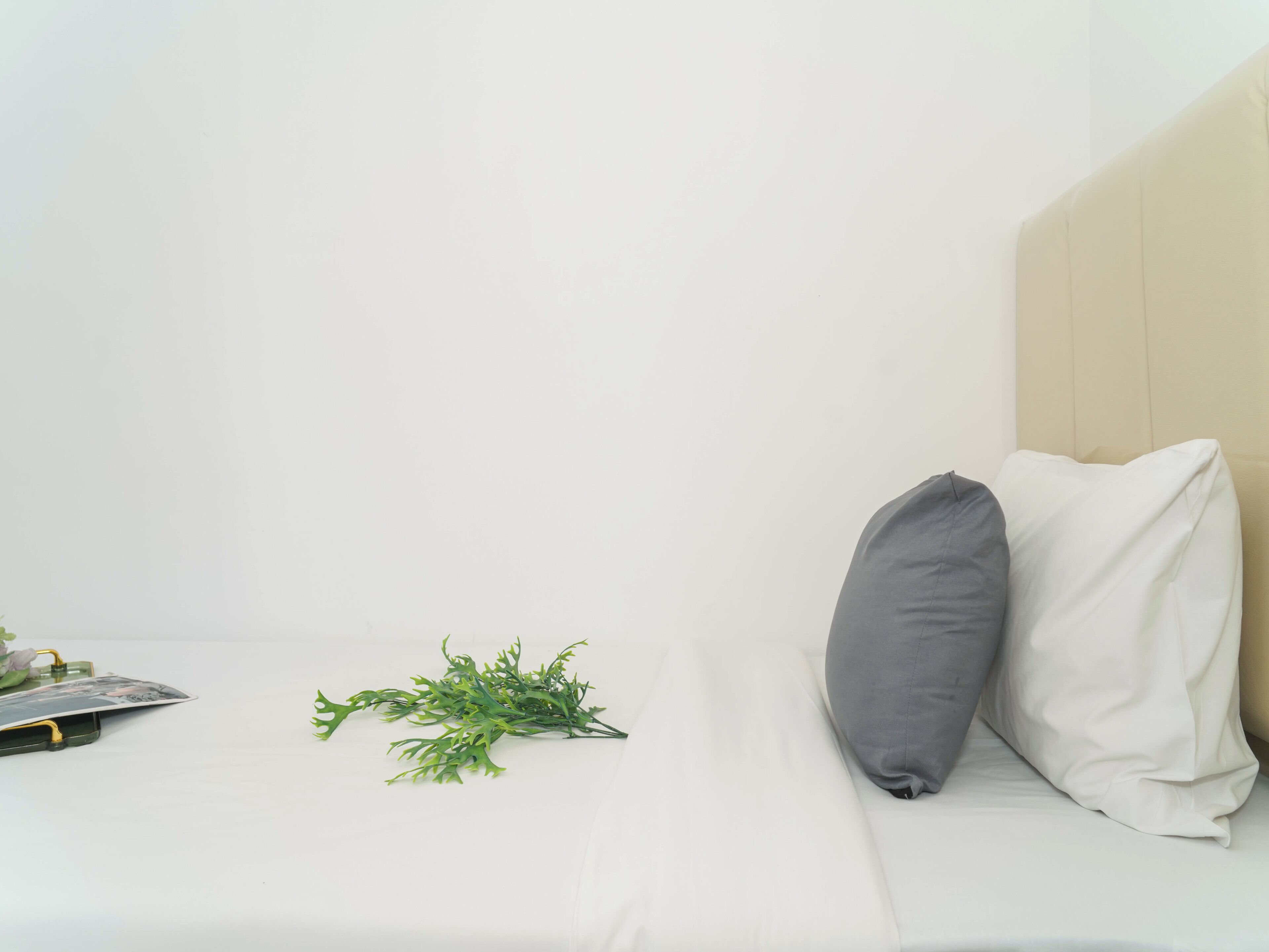 A bed with white bedding, a gray pillow, and a green plant.