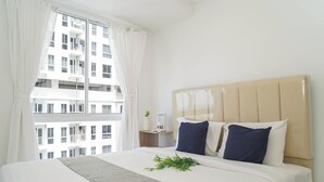 Een hotelkamer met een groot bed, een raam met gordijnen, een nachtkastje met een plant en uitzicht op een gebouw.