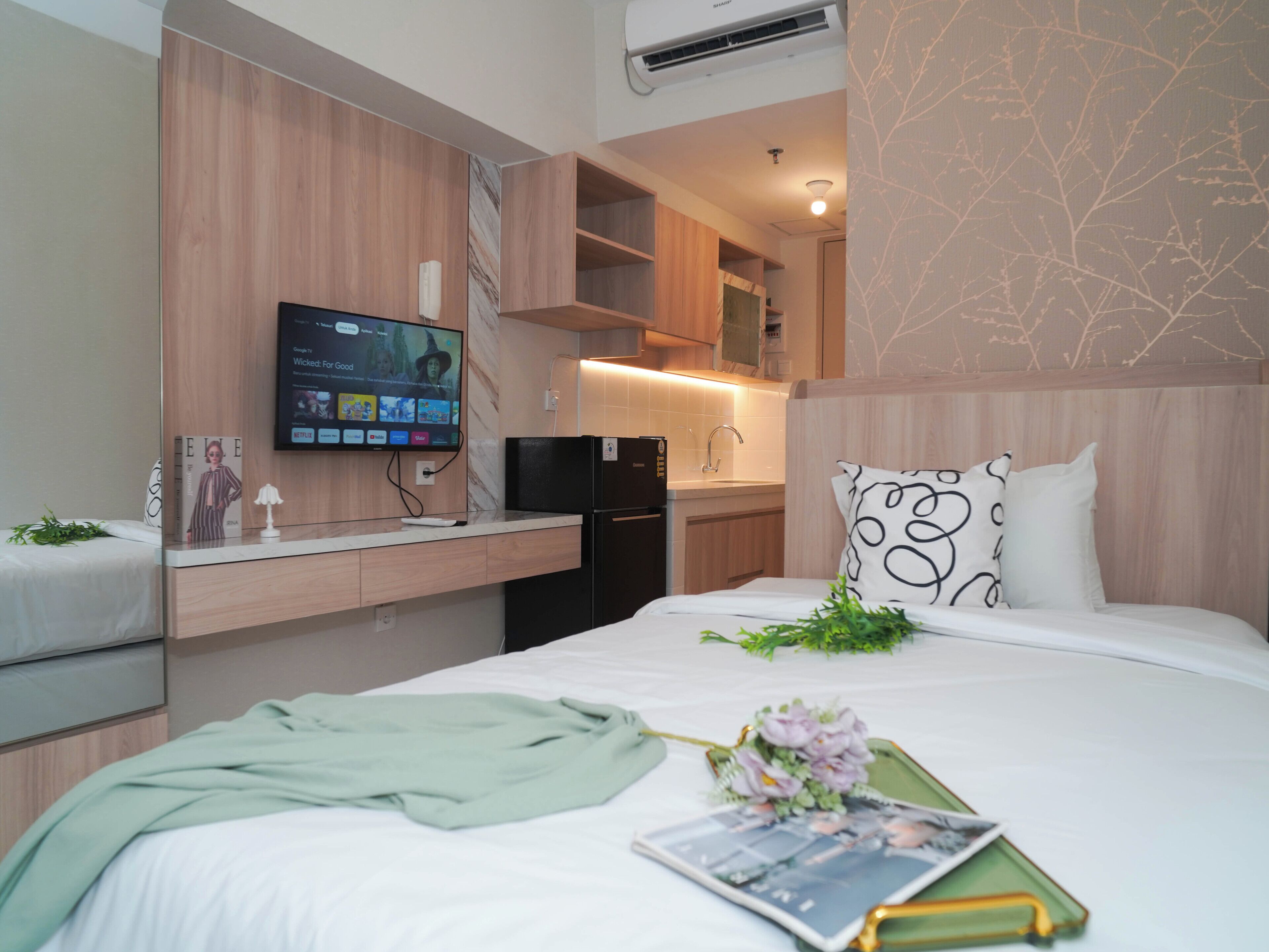 A modern hotel room with a bed, a flat-screen TV, a small kitchenette, and a decorative wall.