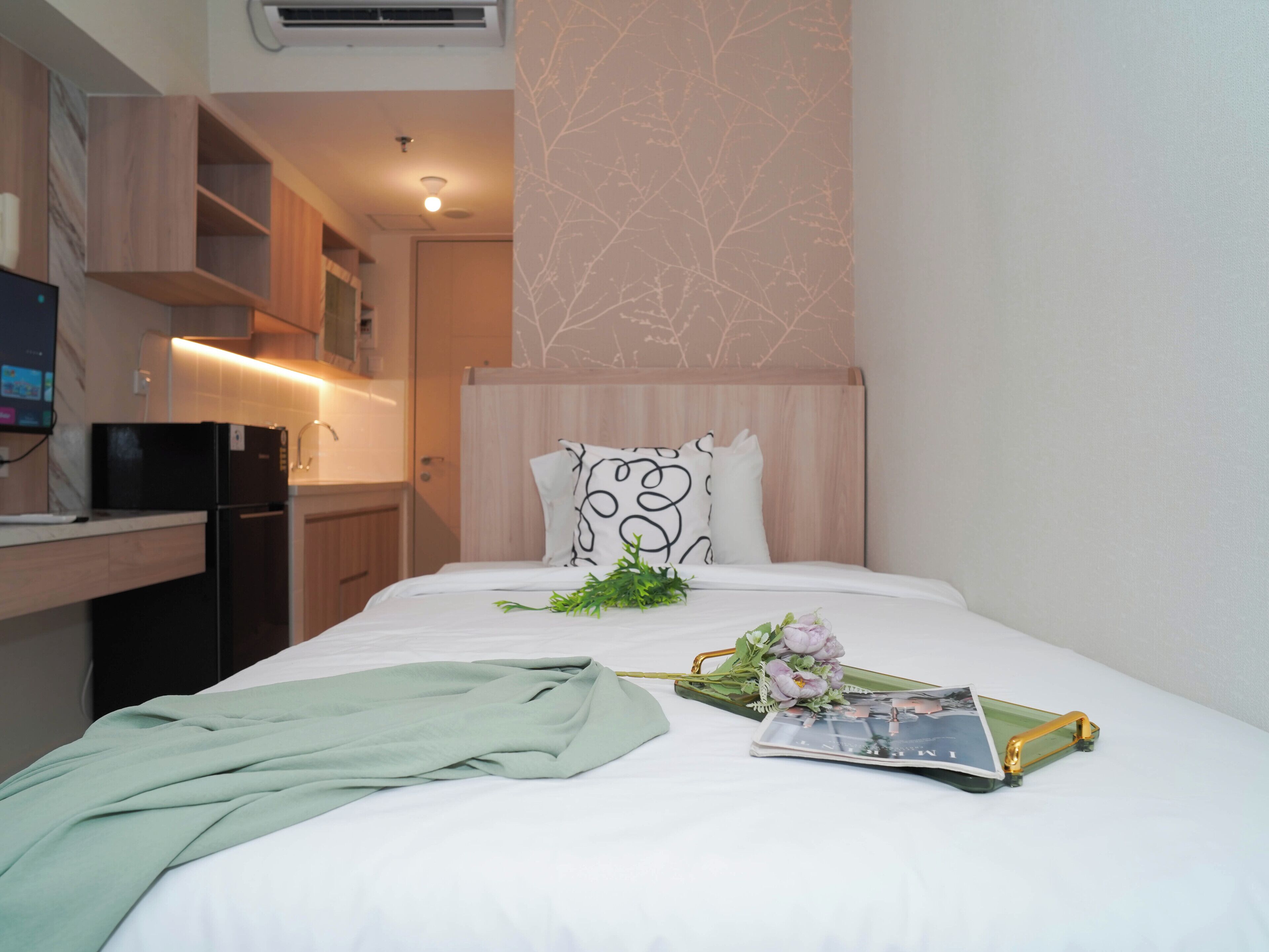 Una habitación de hotel con cama, mesita de noche, escritorio con computadora y kitchenette.