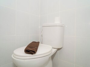 Eine weiße Toilette mit einem braunen Handtuch auf dem Deckel, vor einer gefliesten Wand.