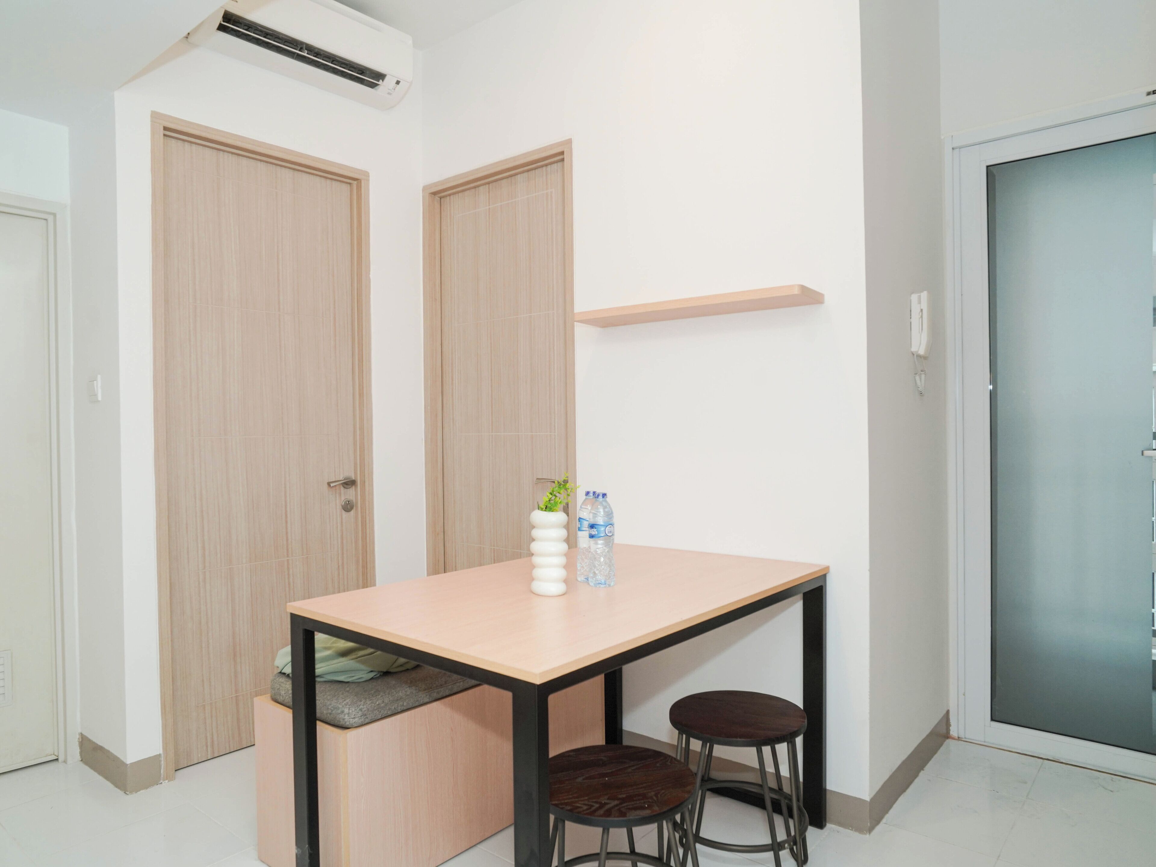 A small room with a table, two stools, a water bottle, and a plant on the table.