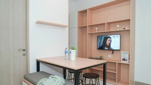 Ein modernes Zimmer mit Schreibtisch aus Holz, einer Sitzbank, einem an der Wand befestigten Fernseher und einem Bücherregal.