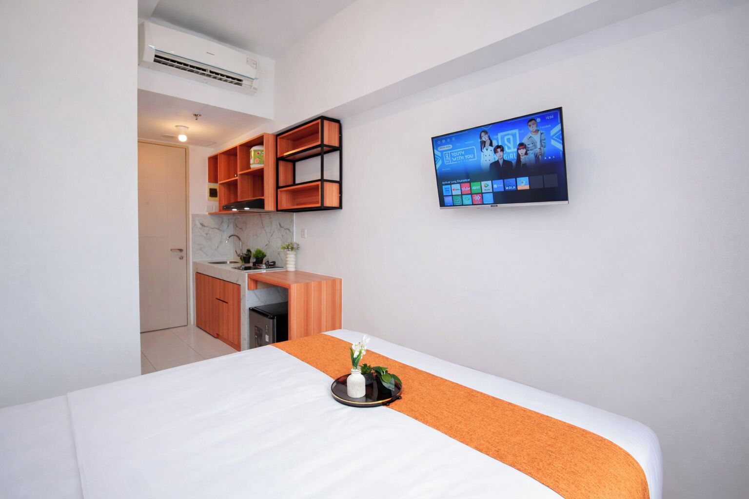 A hotel room with a bed, a small kitchenette, and a TV mounted on the wall.
