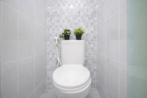 A small, modern bathroom with a toilet, two potted plants, and a tiled wall. - Neat And Minimalist Studio At Tokyo Riverside Pik 2 Apartment Near Tokyo Hub (Teluknaga)