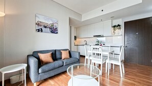A modern living space with a sofa, a glass coffee table, a dining table with chairs, and a kitchen area. - Cozy Living 3Br At Transpark Bintaro Apartment (South Tangerang)