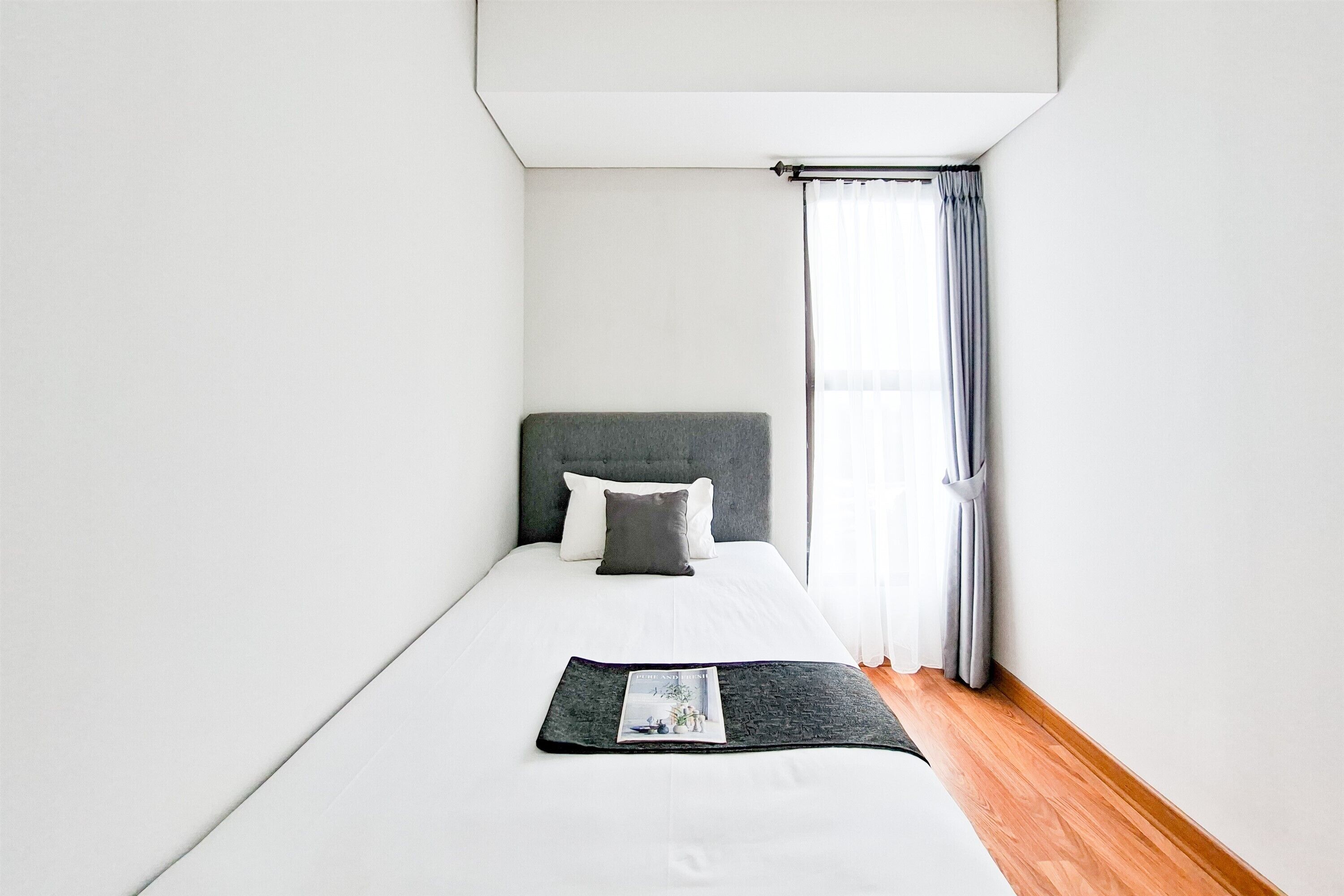 Un dormitorio con cama, una ventana con cortinas y una revista sobre la cama.