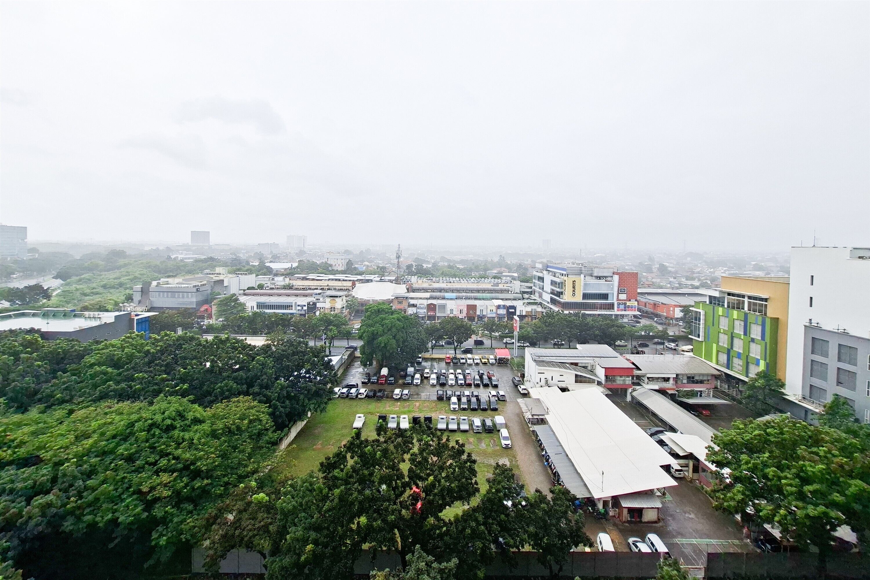 An aerial view of a cityscape with buildings, a parking lot, and greenery.