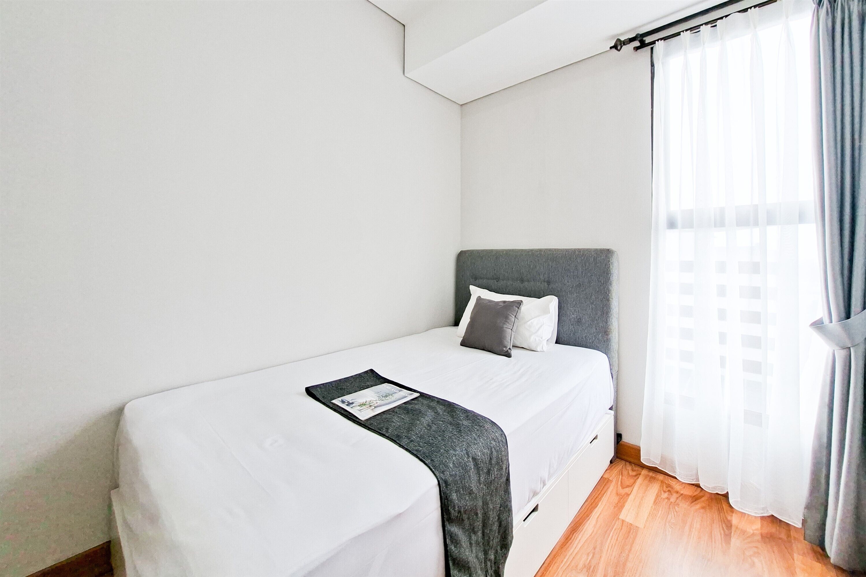 A single bed with a grey headboard, white bedding, and a grey throw blanket.