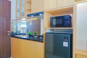 A compact kitchen with wooden cabinets, a stainless steel refrigerator, a microwave, and a gas stove. - Soft Toned Studio At Transpark Cibubur Apartment (Depok)