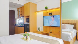A hotel room with a bed, a TV, a kitchenette, and a wooden wardrobe. - Soft Toned Studio At Transpark Cibubur Apartment (Depok)
