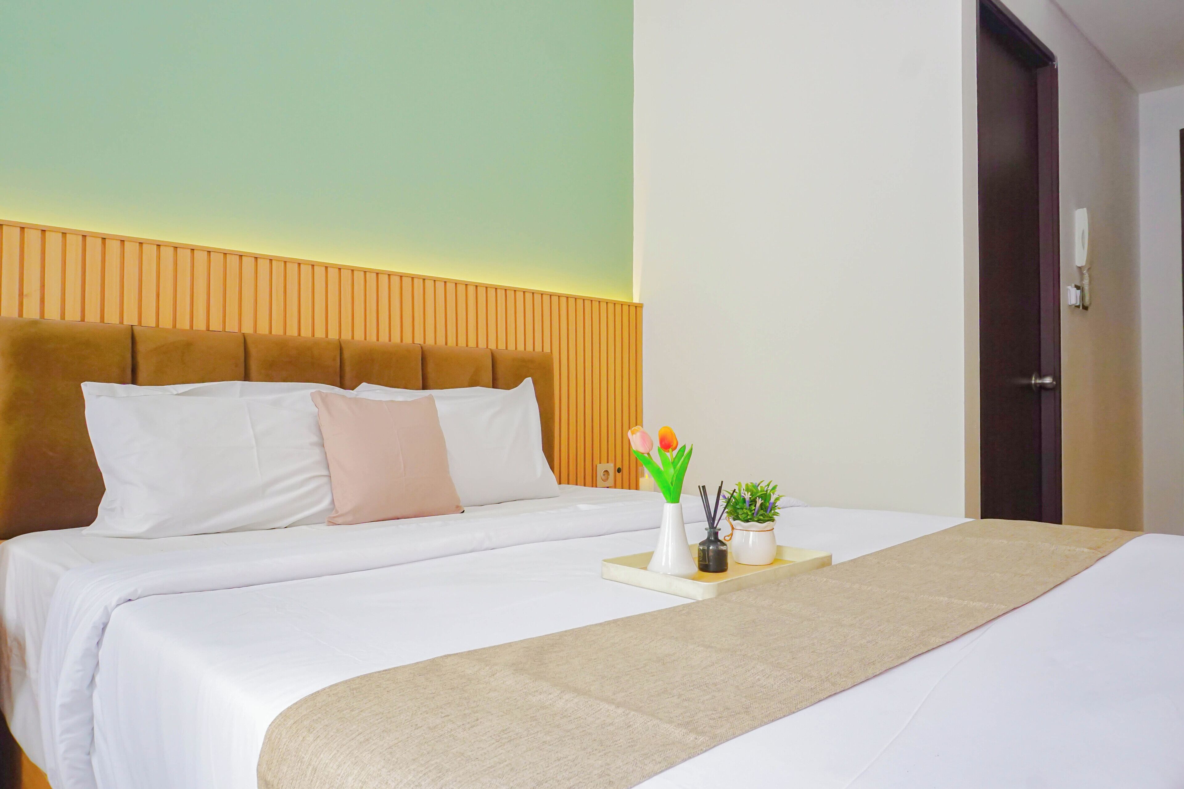 A hotel room with a bed, a bedside table with a vase and a plant, and a wooden headboard.