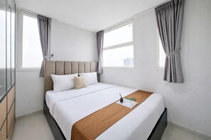 A modern hotel room with a large bed, a headboard, a bedside table with a lamp, and a window with curtains. - Comfy White 2Br For 3 Pax At Tuscany Residence (South Tangerang)
