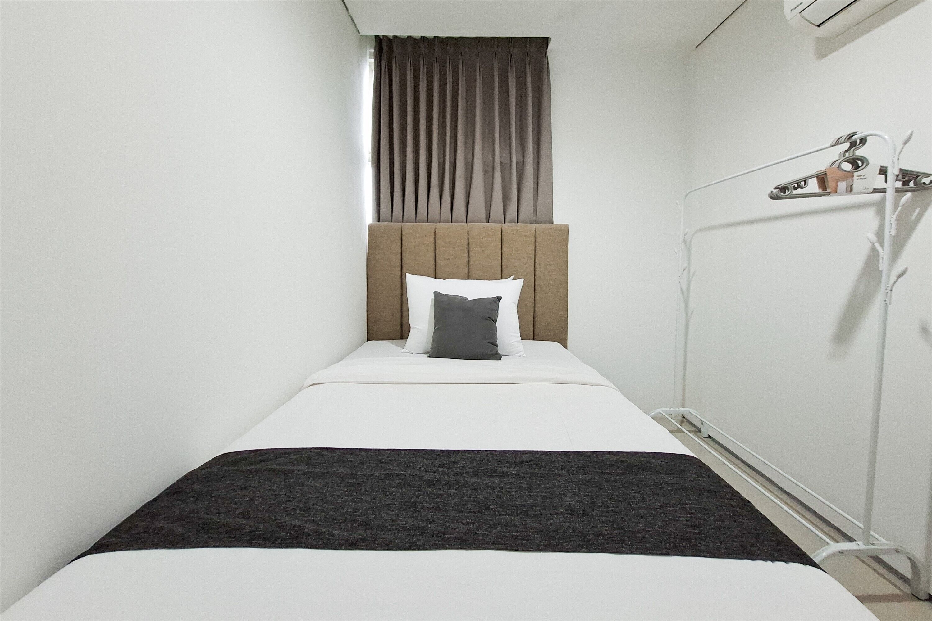 A single bed with a headboard, a bedside table, a hanging light, and a window with curtains.