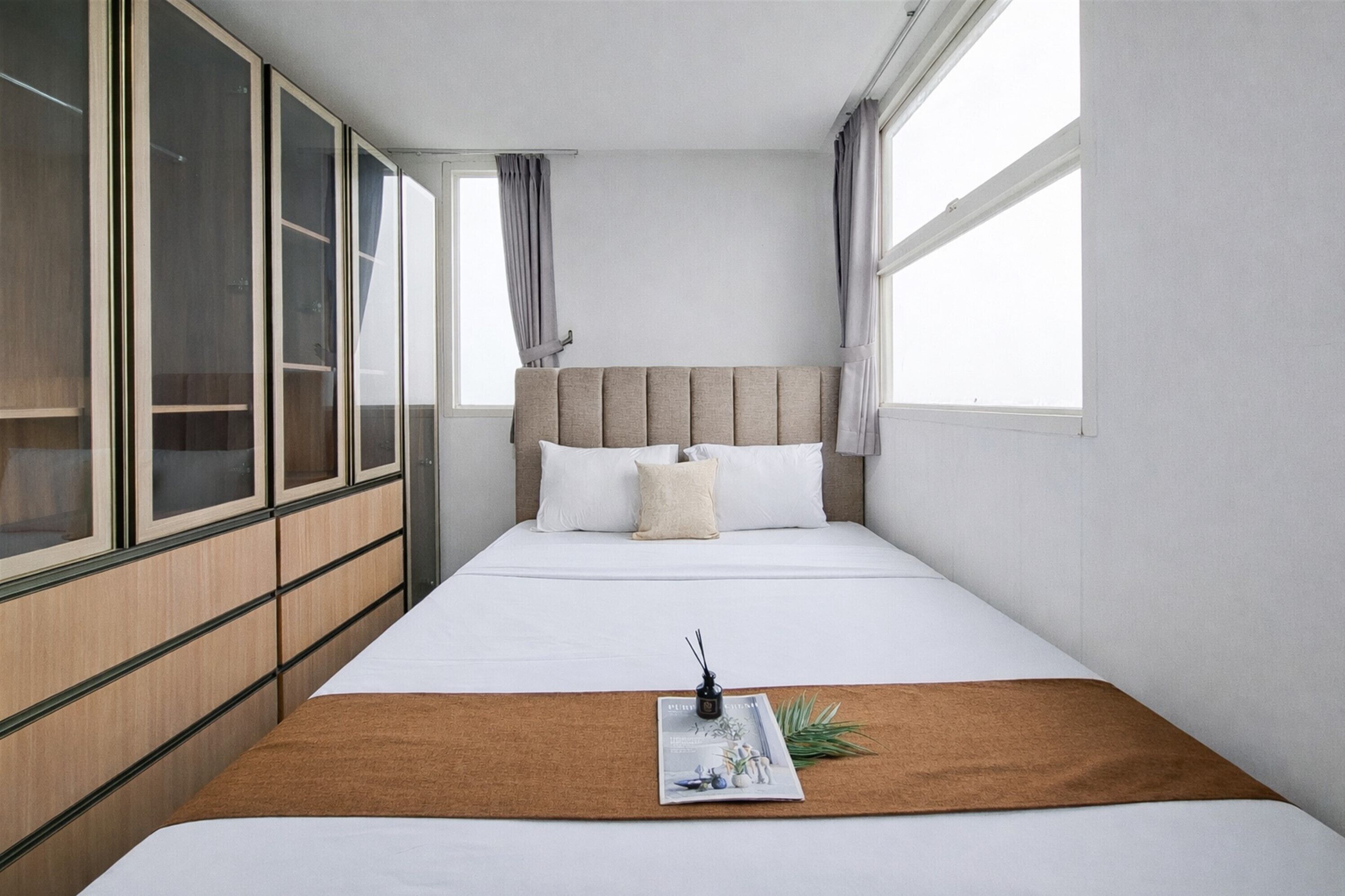Une chambre d’hôtel bien rangée, avec un lit, une table de chevet, un magazine et une fenêtre avec des rideaux.