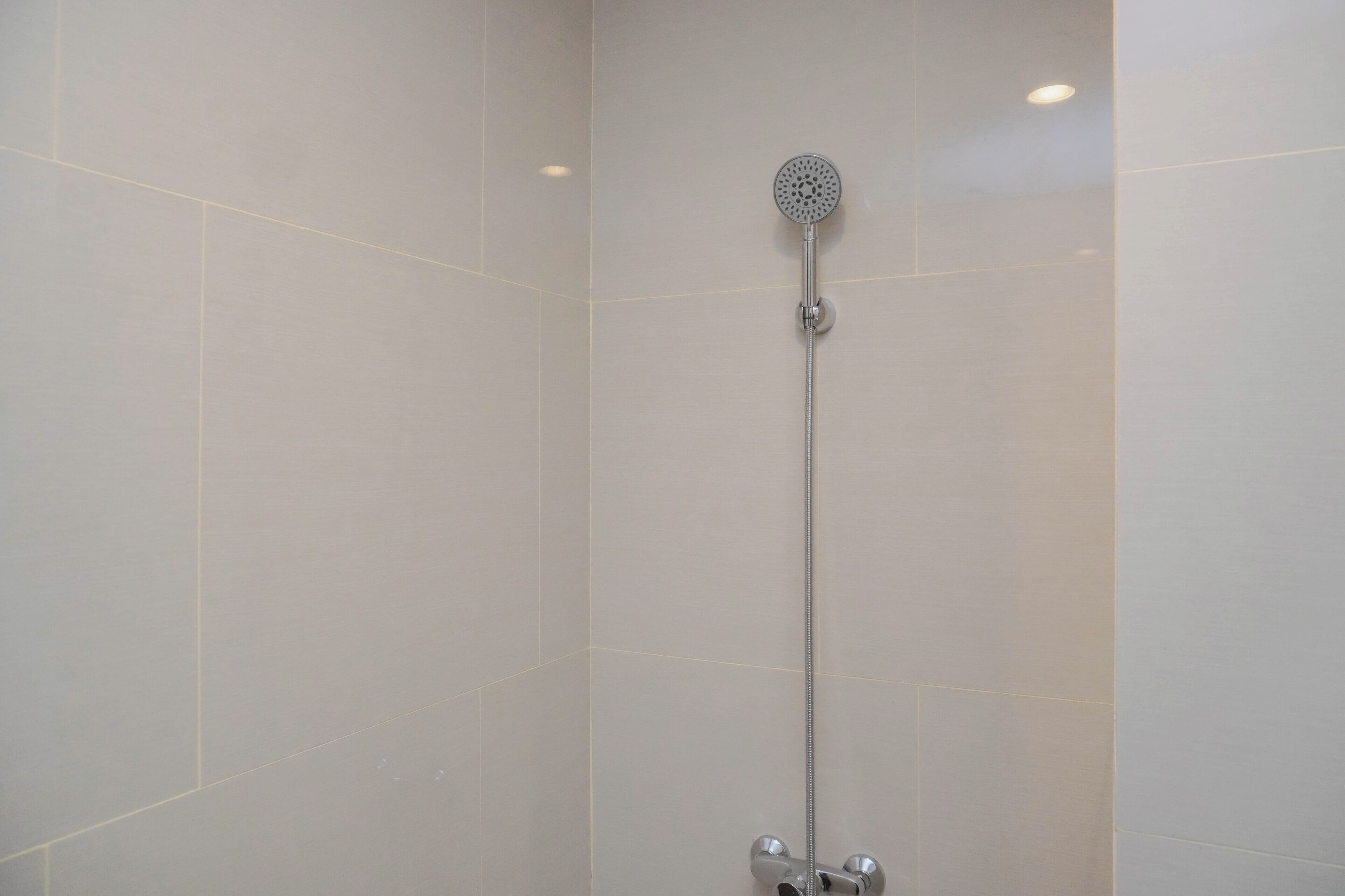 A shower with a handheld showerhead, a wall-mounted control panel, and a single light fixture.