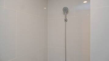 A shower with a handheld showerhead, a wall-mounted control panel, and a single light fixture.