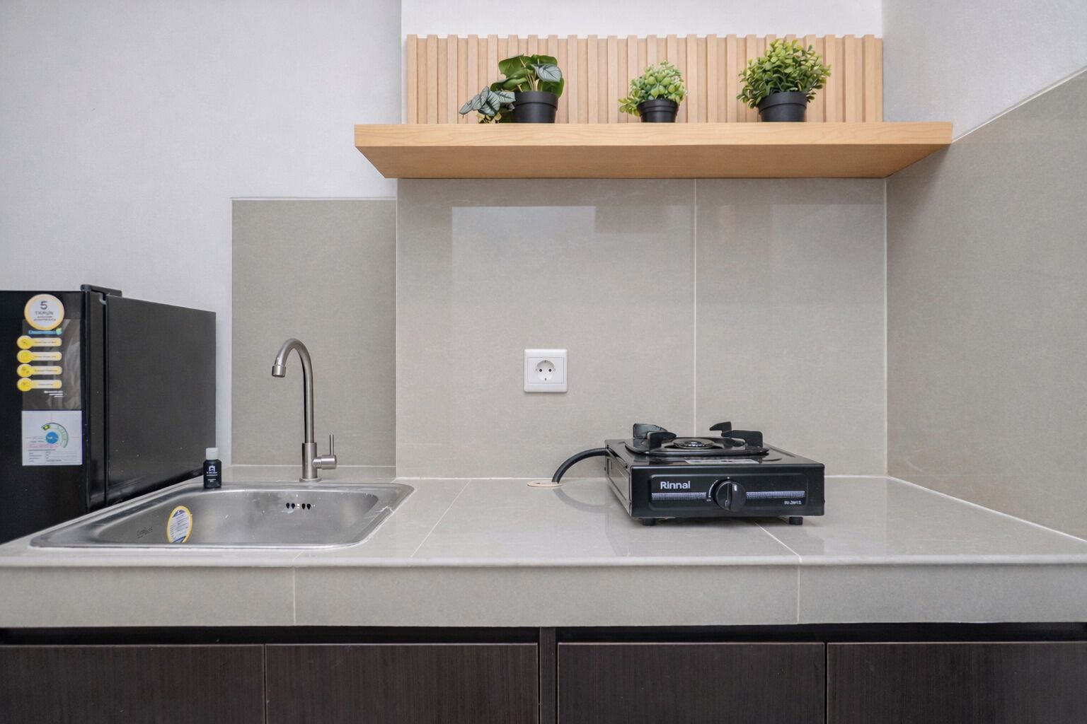 A kitchen with a sink, a stove, a refrigerator, and a wooden shelf with potted plants.