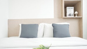 Ein Bett mit Kopfteil, zwei Kissen, ein Nachttisch mit einer Lampe und ein an der Wand hängendes Magazin mit dem Titel 'LOEWE'.