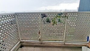 A balcony with perforated metal railings, a small plant, and a view of a cityscape. - Wooden Touch Restful Studio At Apartment West Vista (Jakarta)