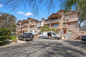 A multi-story hotel with balconies, a parking area, and a van parked in front. - Harborside 201: Charming Condo Steps from the Beach (Myrtle Beach)