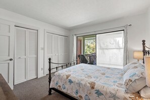 A bedroom with a bed, a window with curtains, a door, and a chair. - Harborside 201: Charming Condo Steps from the Beach (Myrtle Beach)