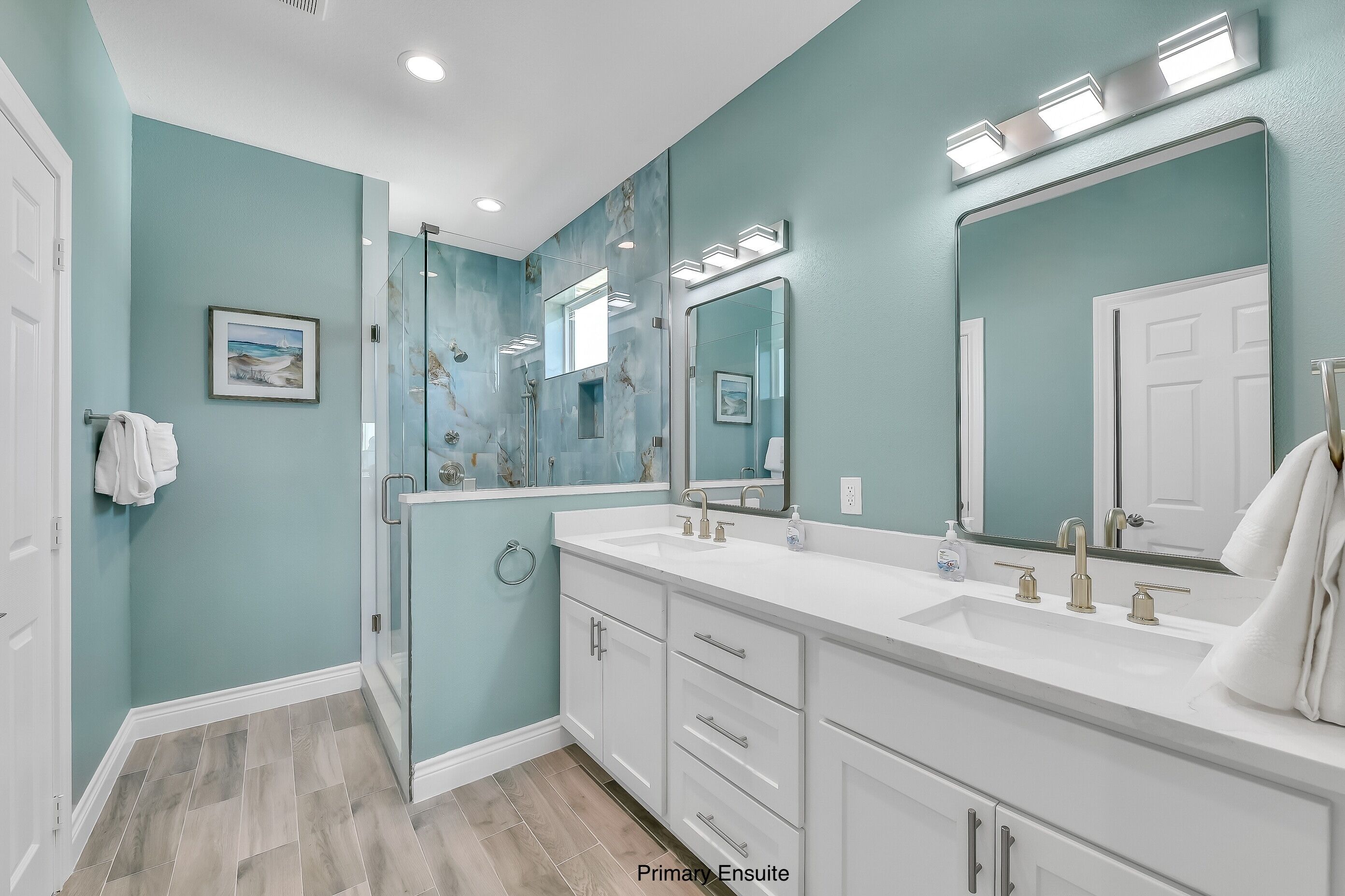 A modern bathroom with teal walls, a double sink vanity, and a glass shower enclosure.