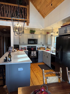 A modern kitchen with white cabinets, a black refrigerator, a microwave, and a wooden dining table with chairs.