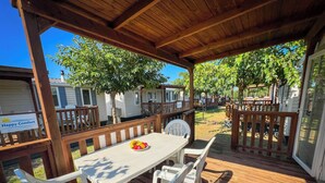Un espace extérieur abrité, doté d’une table de pique-nique et de chaises, entouré de clôtures en bois et d’arbres.