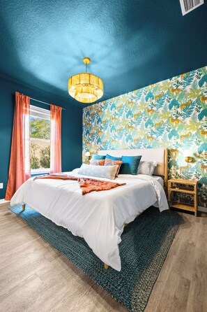 Une chambre avec un grand lit, une table de chevet en bois, un mur à motifs et une fenêtre avec des rideaux.