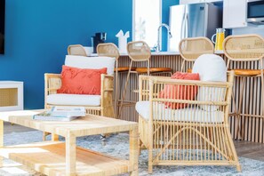 Un salon moderne avec des meubles en osier, une table basse et un coin cuisine à l’arrière-plan.