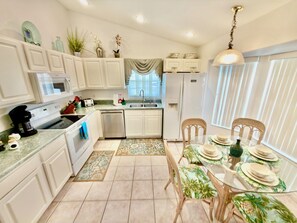 A kitchen with white cabinets, a microwave, a stove, a dishwasher, and a dining area with a table set for two. - 4 miles to Disney, 4 bed. Private Pool +Spa. King Triton’s Theme,  Free Snacks. (Kissimmee)