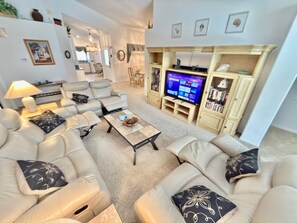 A living room with a sofa set, a coffee table, a television, and a bookshelf. - 4 miles to Disney, 4 bed. Private Pool +Spa. King Triton’s Theme,  Free Snacks. (Kissimmee)