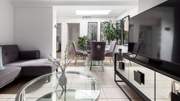 Ein modernes Wohnzimmer mit einer Couch, einem Glastisch, einem Fernseher und einem Essbereich mit Stühlen und Tisch.