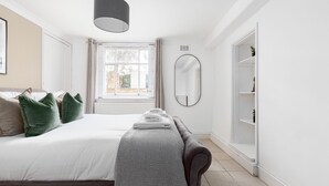 Ein Schlafzimmer mit Bett, Nachttisch, Spiegel und Fenster.