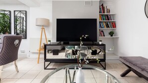 Ein modernes Wohnzimmer mit Fernseher, Bücherregal, Glastisch mit Vase, Sessel und Bank.