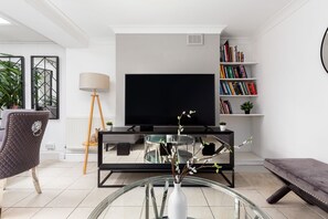 Ein modernes Wohnzimmer mit Fernseher, Bücherregal, Glastisch mit Vase, Sessel und Bank.