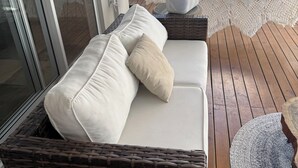 Een rieten bank met kussens op een houten terras, een hangmat en een mand met handdoeken.
