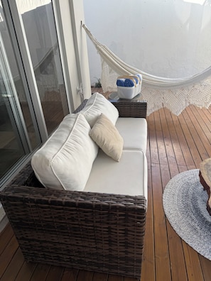 A wicker sofa with cushions on a wooden deck, a hammock, and a basket with towels. - Juquehy Corner (São Sebastião)