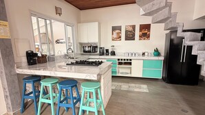 Een moderne keuken met een centraal eiland, een paar barkrukken, een ingebouwde kookplaat en een spiltrap.