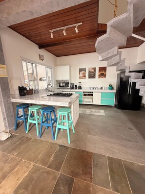 A modern kitchen with a central island, bar stools, a built-in stove, and a spiral staircase. - Juquehy Corner (São Sebastião)