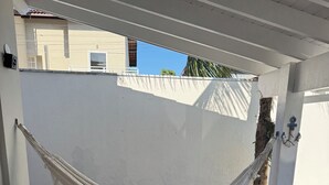Een hangmat onder een wit plafond, een witte bank met kussens, en een houten terras.