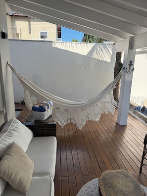 A hammock under a white ceiling, a white sofa with cushions, and a wooden deck. - Juquehy Corner (São Sebastião)