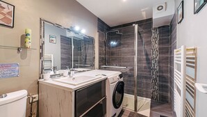 Uma casa de banho moderna com cabine de duche em vidro, máquina de lavar e um espelho grande.