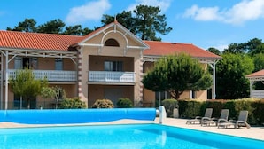 A hotel with a swimming pool, a covered outdoor area, and a two-story building with balconies. - Apartment in Soulac-sur-mer Near Beach (Soulac-sur-Mer)