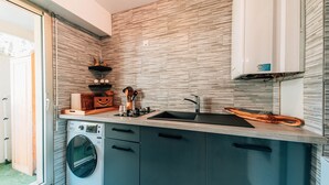 Eine kleine Küche mit Waschmaschine, Spüle und Schneidebrett aus Holz.