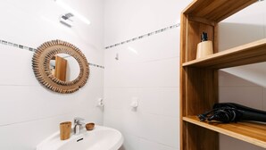 Ein Badezimmer mit einem weißen Waschbecken, einer Holztrennwand und einem Spiegel mit geflochtenem Rahmen.